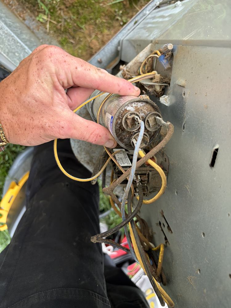 Technician inspecting a run capacitor at the condenser's electrical compartment